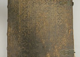 Die Bibel ist ein großes Buch. Der Einband ist aus Leder. Das Leder ist verziert. Die Ecken des Einbandes haben Metallkappen. Die Kappen schützen den Einband.
