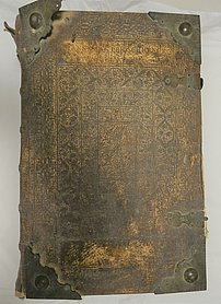 Die Bibel ist ein großes Buch. Der Einband ist aus Leder. Das Leder ist verziert. Die Ecken des Einbandes haben Metallkappen. Die Kappen schützen den Einband.