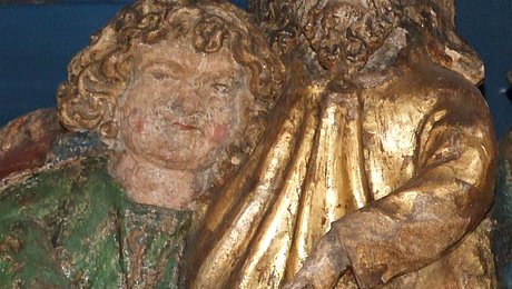 FFM_Wovon_wir_leben_koennen Fotoaufnahme einer figürlichen Darstellung des Abendmahls. Bei der Figur rechts mit Bart und Heiligenschein handelt es wohl um Jesus. Er gestikuliert mit seiner Hand in Richtung des Brotes, das auf dem Tisch vor ihm liegt. Die Figur links ist kleiner und lehnt sich an Christus an.